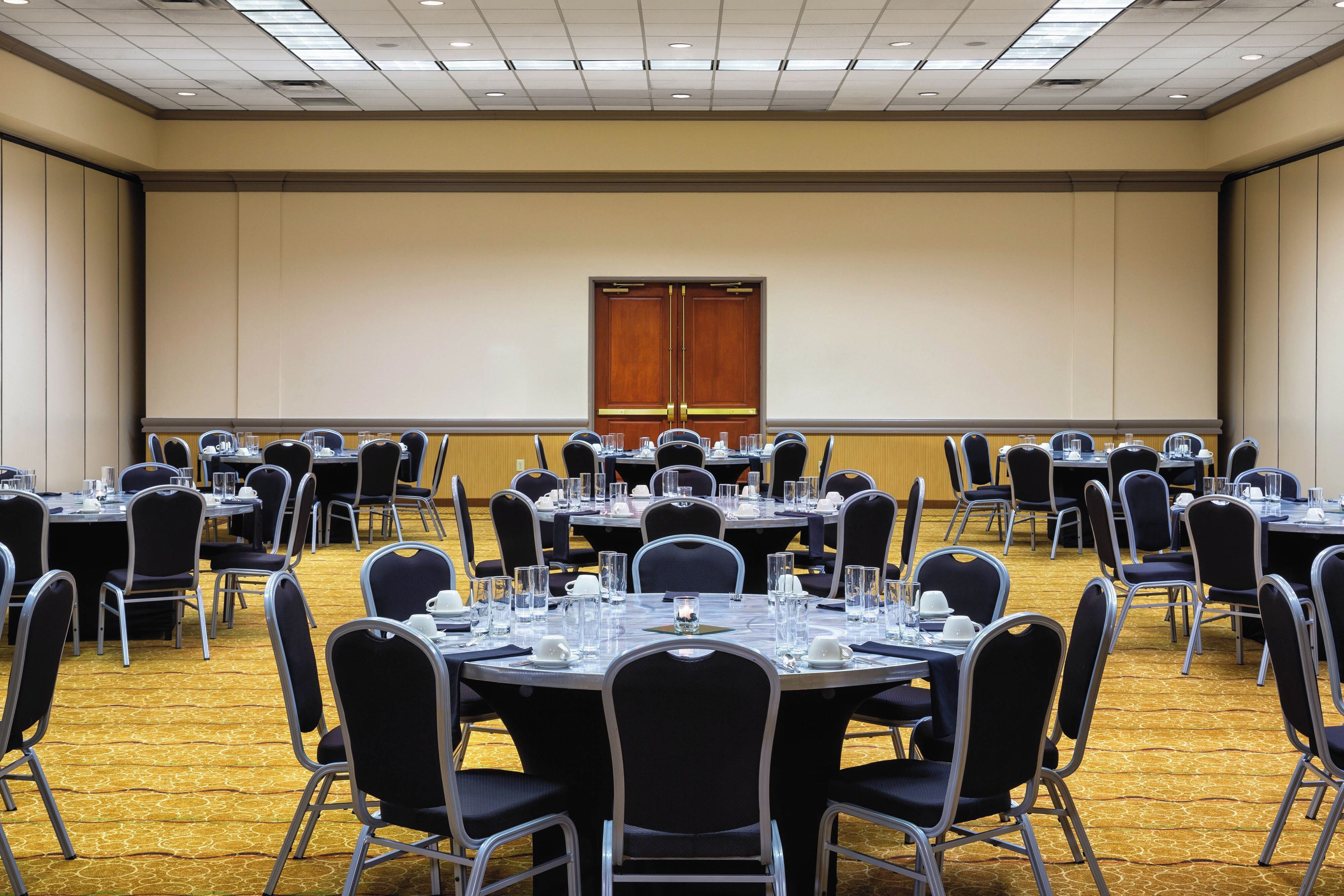 A conference room with multiple round tables, each set with chairs, glasses, and cutlery.