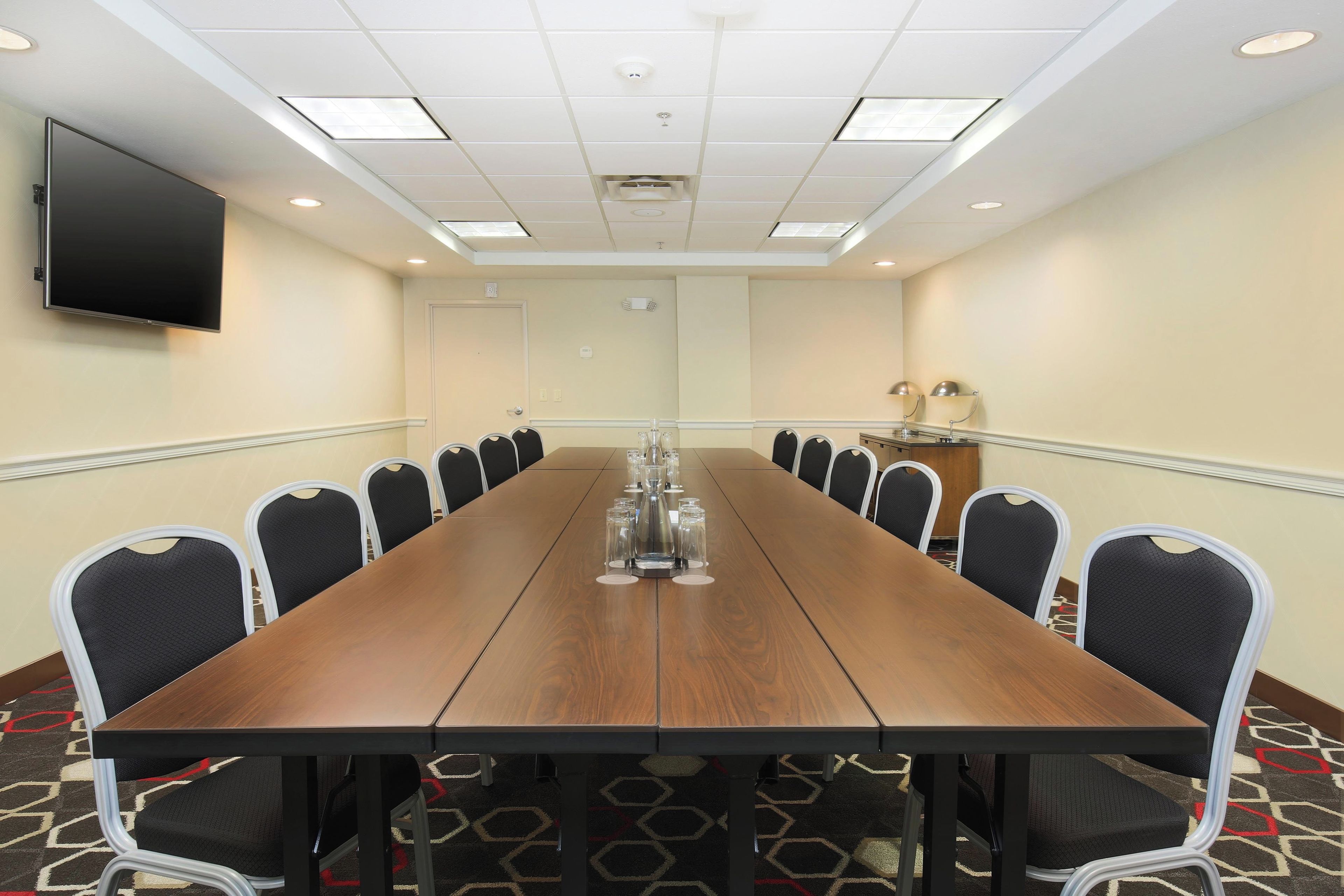 A conference room with a long table, chairs, a flat-screen TV, and a carpeted floor.