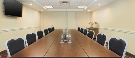 A conference room with a long table, chairs, a flat-screen TV, and a carpeted floor.