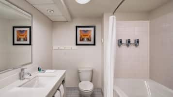 Une salle de bain avec un lavabo blanc, un miroir, des toilettes et une baignoire. Des tableaux encadrés ornent le mur, et il y a un rideau de douche.