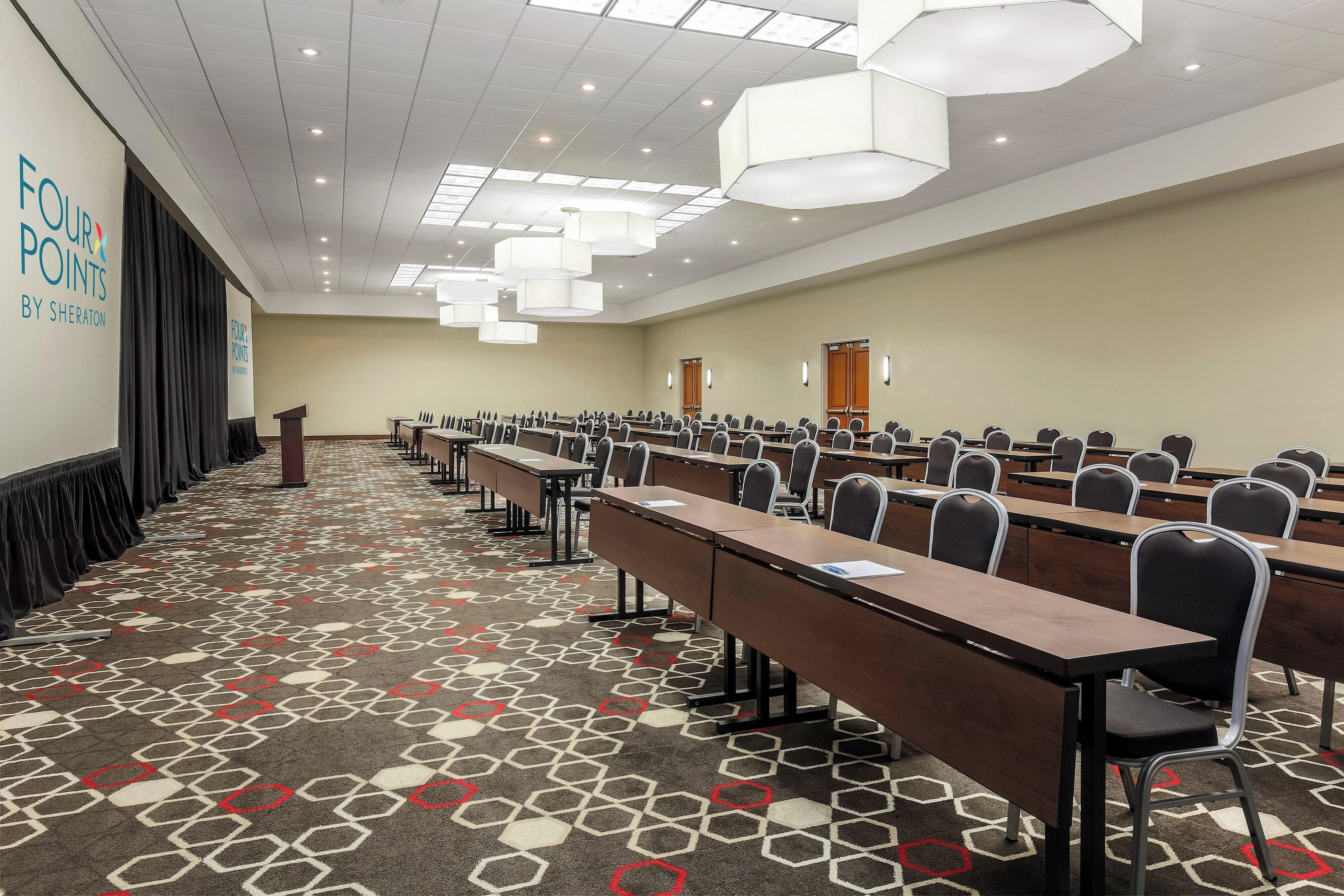 A conference room with rows of tables and chairs, a podium, and a presentation screen.