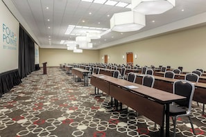 Un salón de conferencias con mesas y sillas dispuestas en filas, un atril y una pantalla de proyecciones.