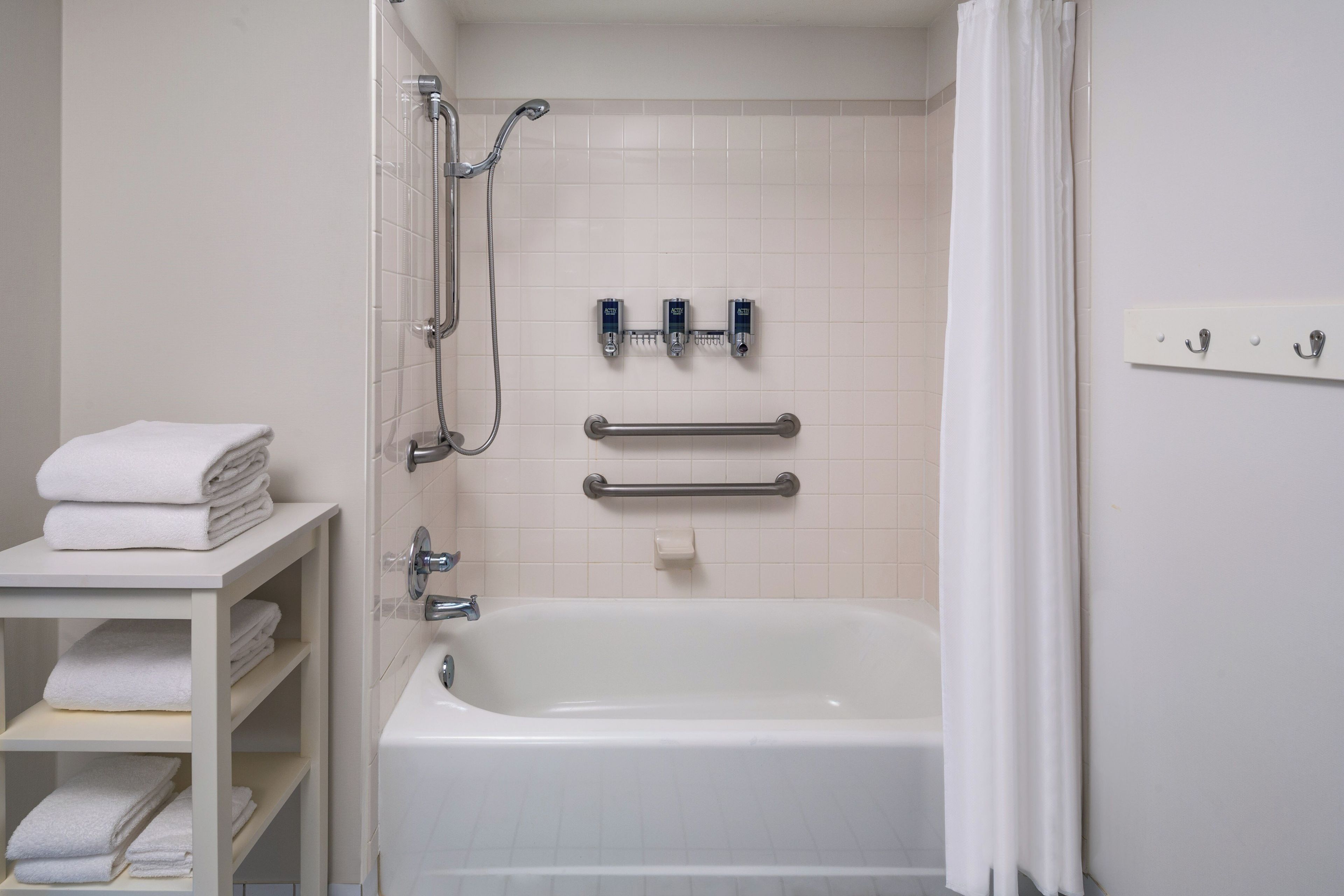 A bathroom with a white bathtub, a shower with a handheld showerhead, a grab bar, and a towel rack.