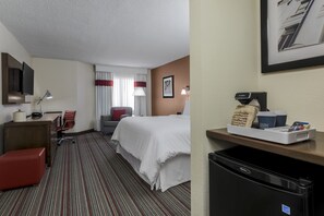 Habitación de hotel con cama, escritorio, silla, lámpara y cafetera.