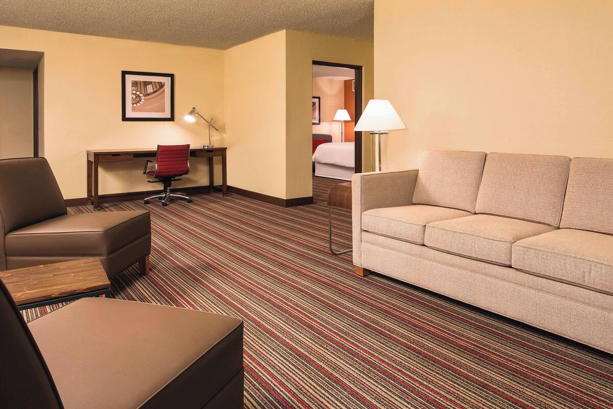 A hotel room with a sofa, a chair, a desk, and a lamp.