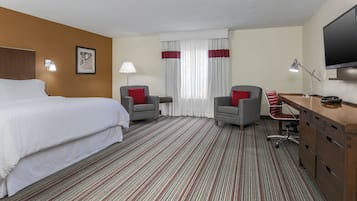 A hotel room with a bed, two armchairs, a desk, a TV, and a window with curtains.