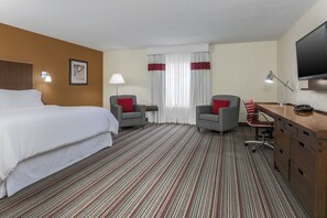 Una habitación de hotel con cama, dos sillones, escritorio, televisión y ventana con cortinas.