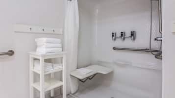 A modern bathroom with a walk-in shower, a white shelf with towels, and a glass shower enclosure.