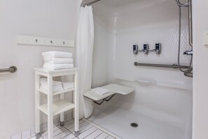 A modern bathroom with a walk-in shower, a white shelf with towels, and a glass shower enclosure. - Four Points by Sheraton Bentonville (Bentonville)