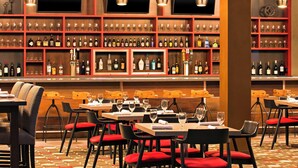 Un restaurante con varias mesas y sillas, una zona de bar con estanterías llenas de botellas, y un televisor colgado en la pared.