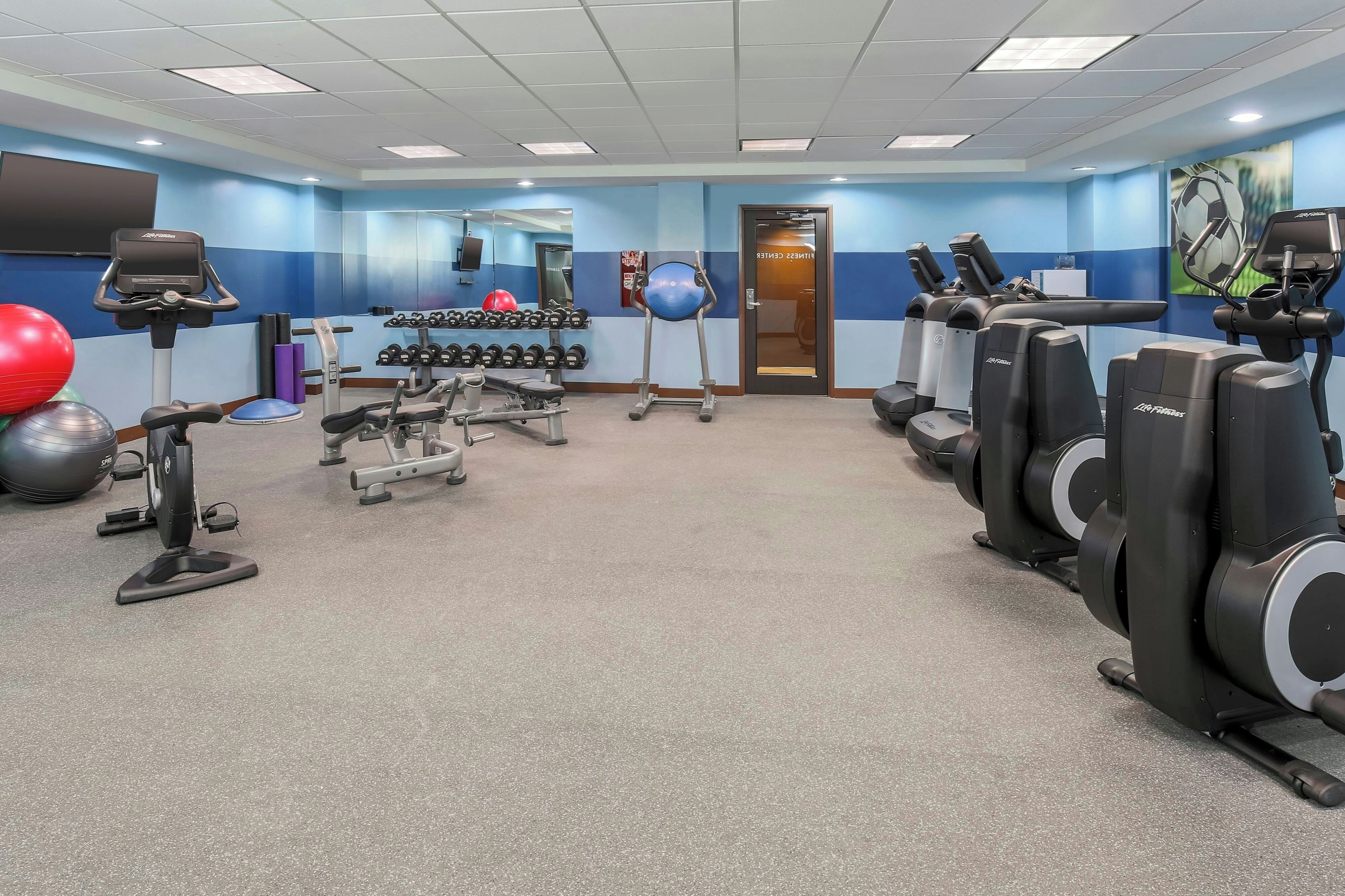 Academia com esteiras, pesos livres e bolas de exercício.