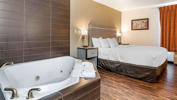 A hotel room with a large bathtub, a bed with white linens, a nightstand with a lamp, and a wall-mounted map.