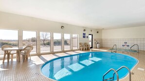 A swimming pool with a tiled floor, a table with chairs, and a view of the outdoors through large windows.