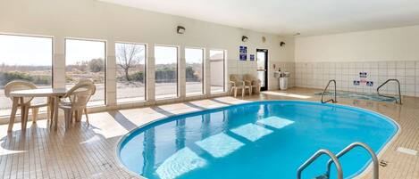 Ein Swimmingpool mit Kachelboden, ein Tisch mit Stühlen und Blick ins Freie durch große Fenster.