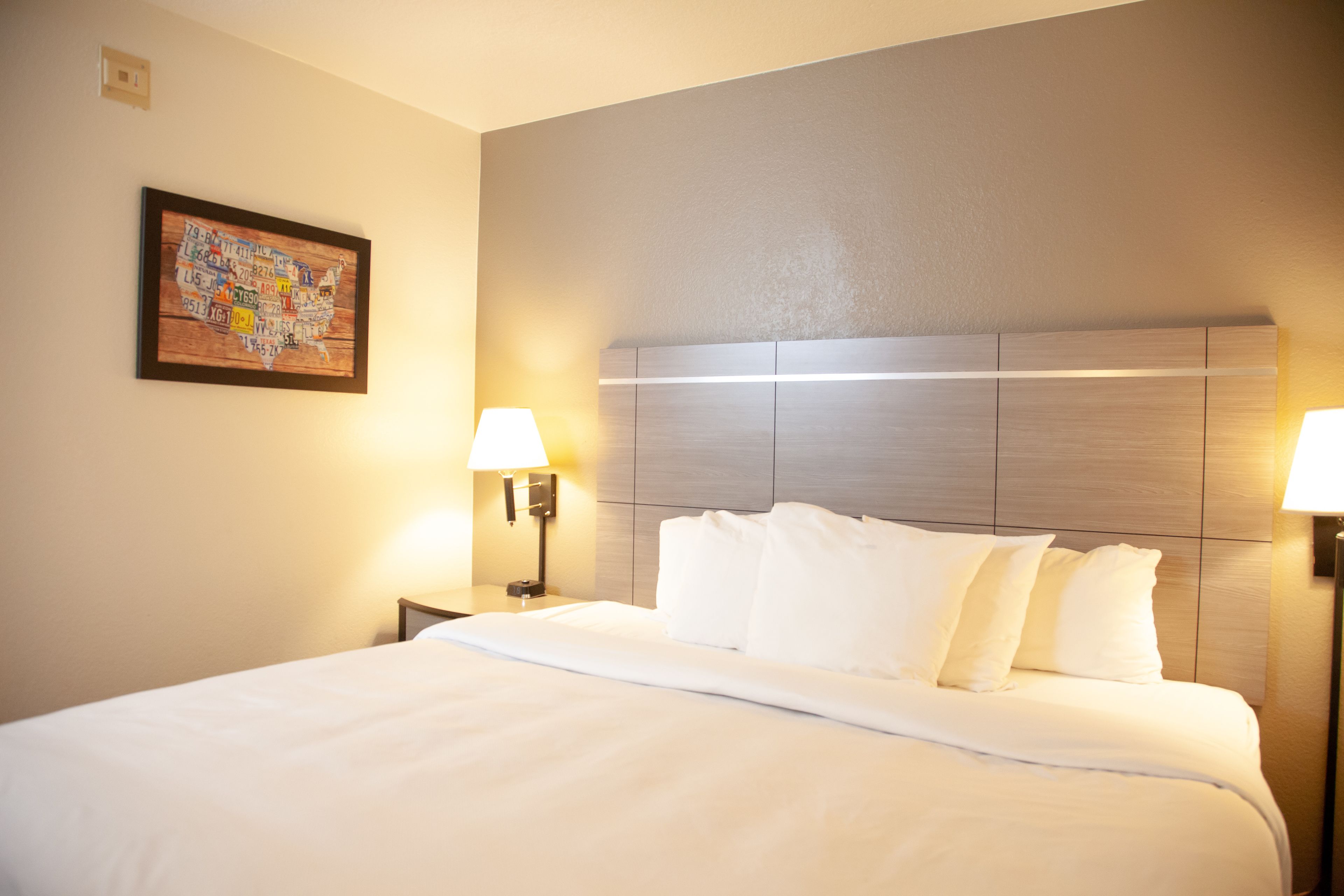Quarto de hotel com uma cama grande, duas luminárias de cabeceira, um encosto de cama e um mapa fixado na parede.