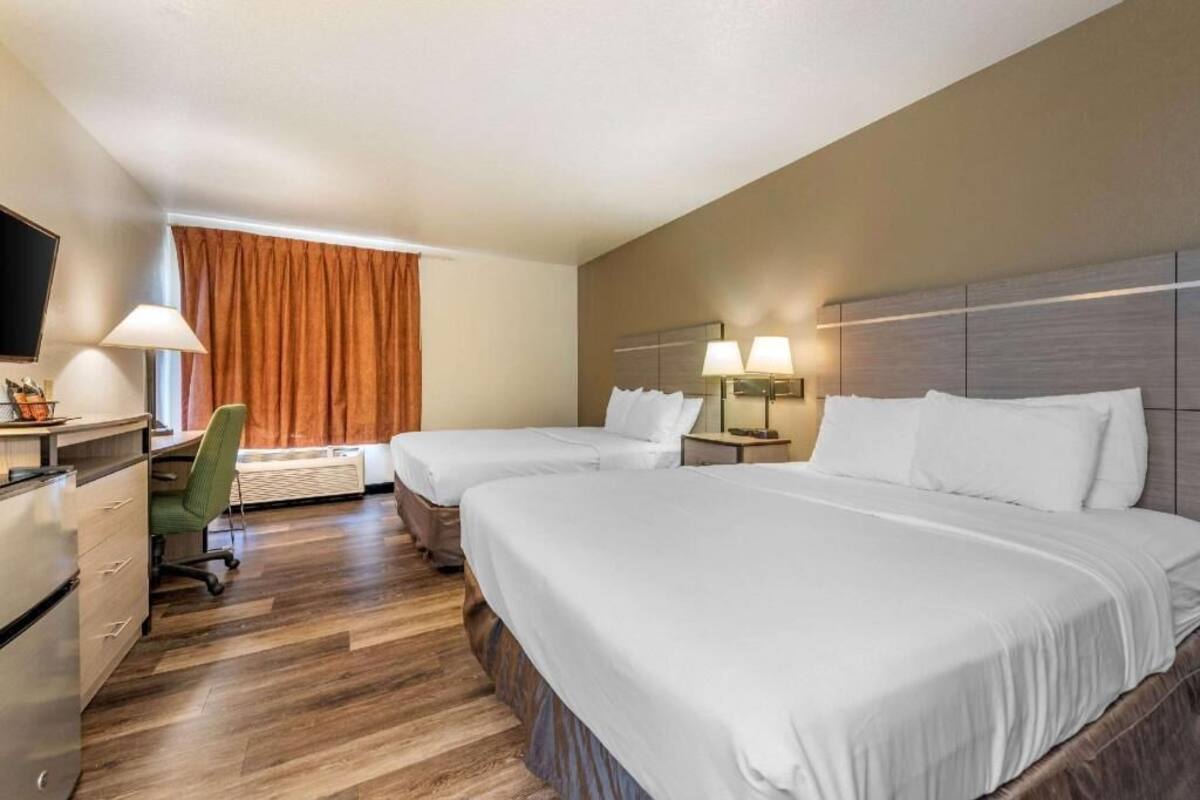 A hotel room with two beds, a desk, a chair, a TV, and a window with curtains.