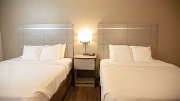Quarto de hotel com duas camas de solteiro, mesa de cabeceira com abajur e cabeceira de madeira.