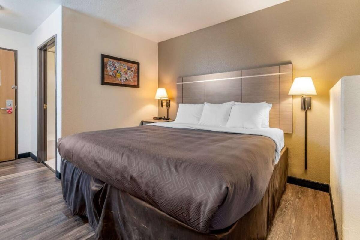 A hotel room with a large bed, two bedside lamps, a headboard, and a door.