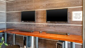 A reception desk with two monitors, a wooden counter, and a sign indicating check-in and check-out times.
