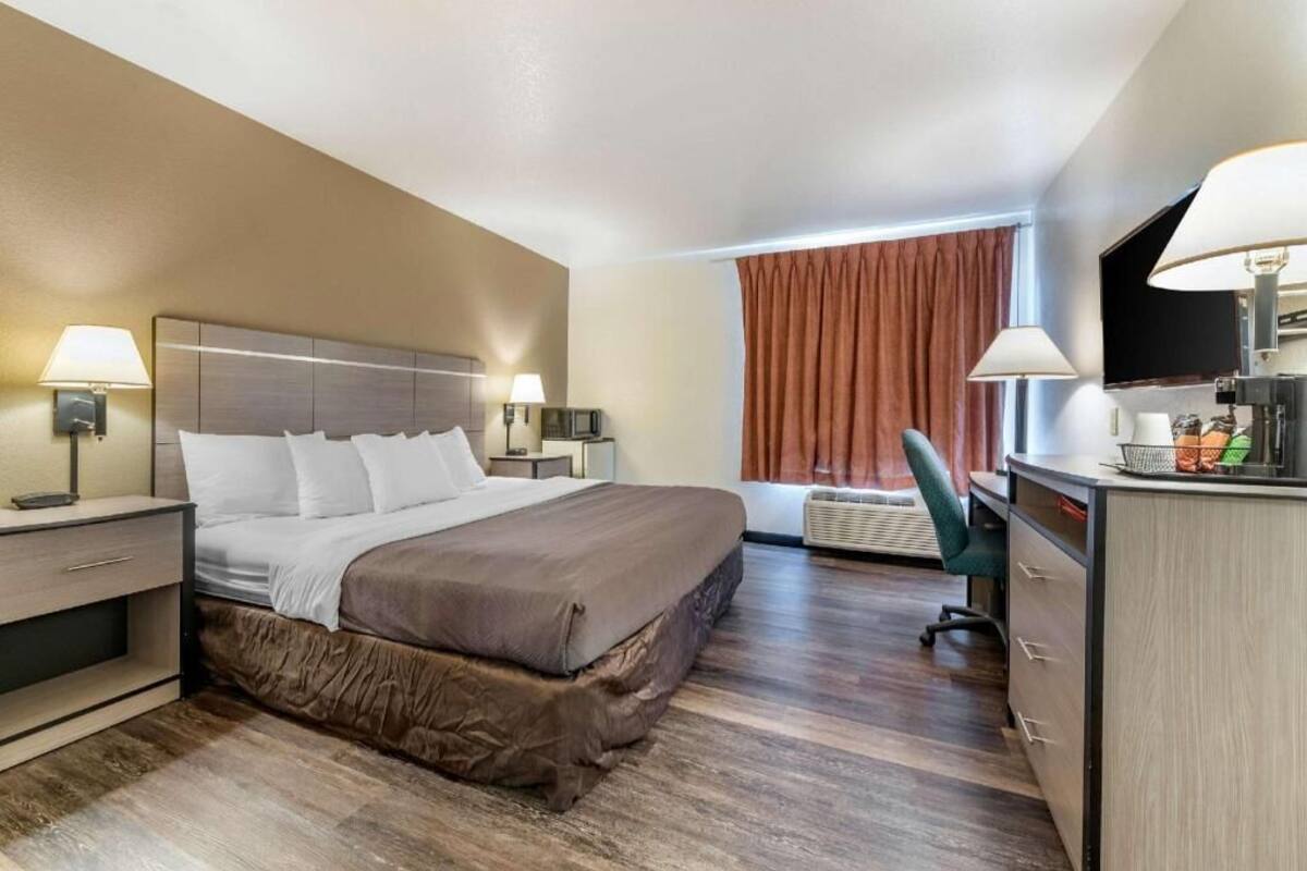 A hotel room with a bed, bedside tables, a desk, a chair, and a television.