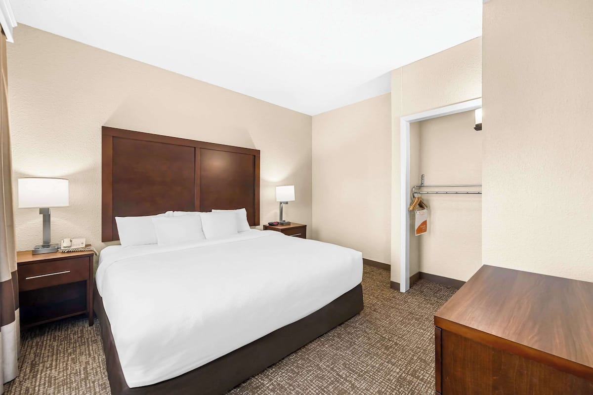 A hotel room with a large bed, two bedside tables with lamps, a wooden headboard, and a door to the right.