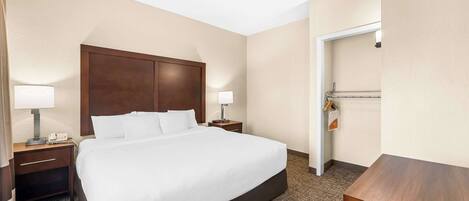 A hotel room with a large bed, two bedside tables with lamps, a wooden headboard, and a door to the right.