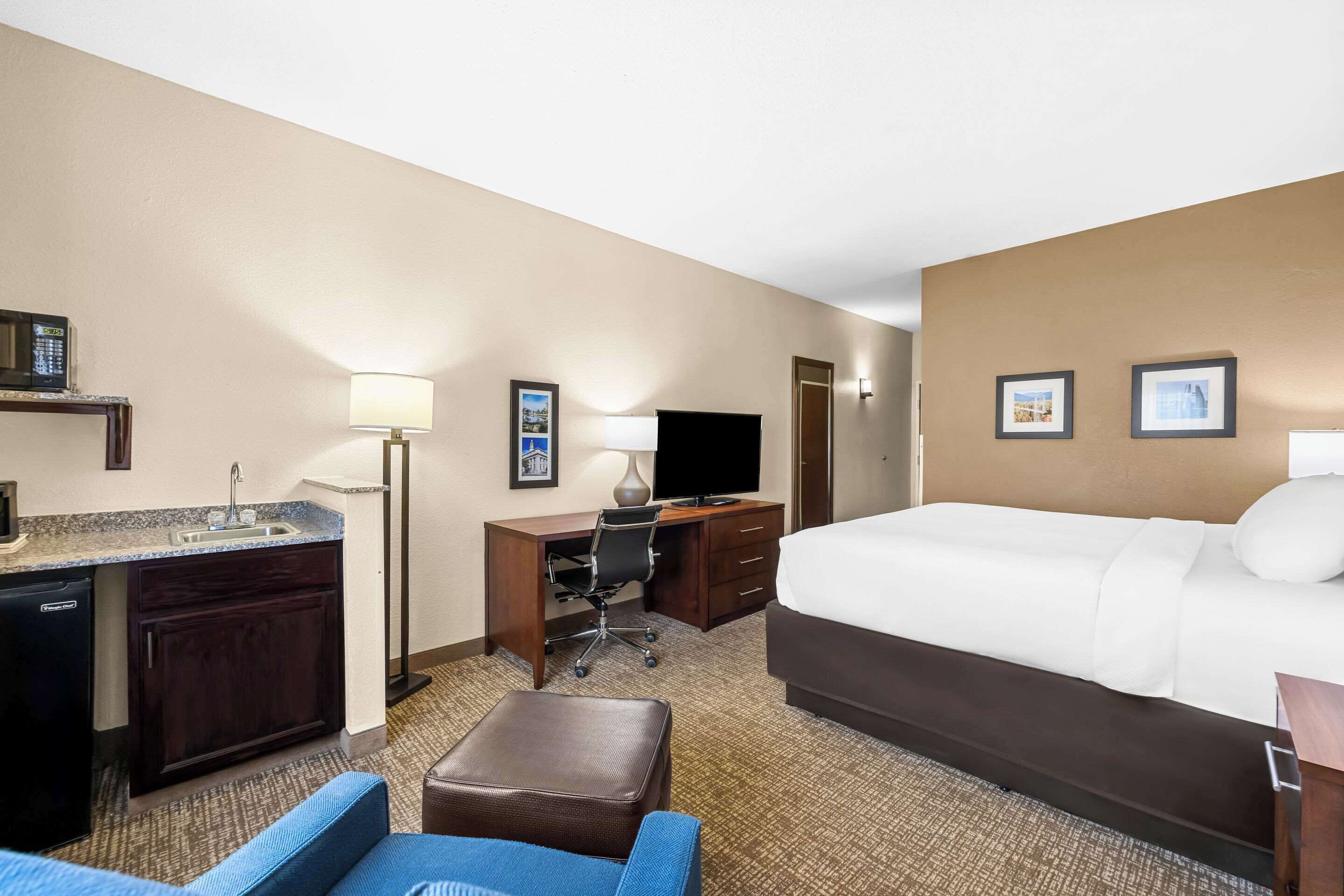 Ein Hotelzimmer mit einem Bett, einem Schreibtisch, einem Stuhl, einer kleinen Küchenzeile und einem Fernseher.