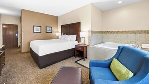 A hotel room with a large bed, a blue armchair, a small table, a desk, a nightstand, a lamp, a telephone, a bathroom with a bathtub, and a shower. - Comfort Inn & Suites Pueblo (Pueblo)