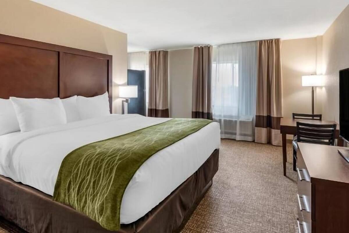 A hotel room with a large bed, a desk, a chair, a TV, and a window with curtains.