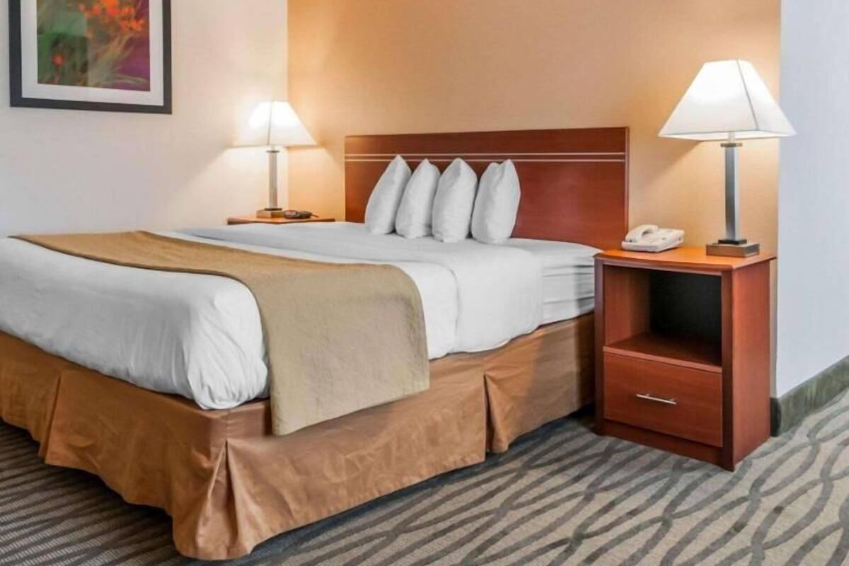 A hotel room with a bed, two bedside lamps, a nightstand with a phone, and a framed picture on the wall.