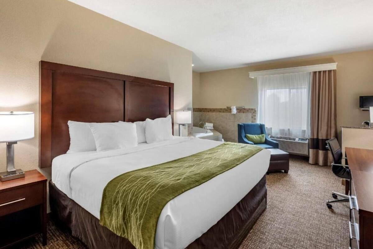 A hotel room with a large bed, a desk, a chair, a TV, and a window with curtains.