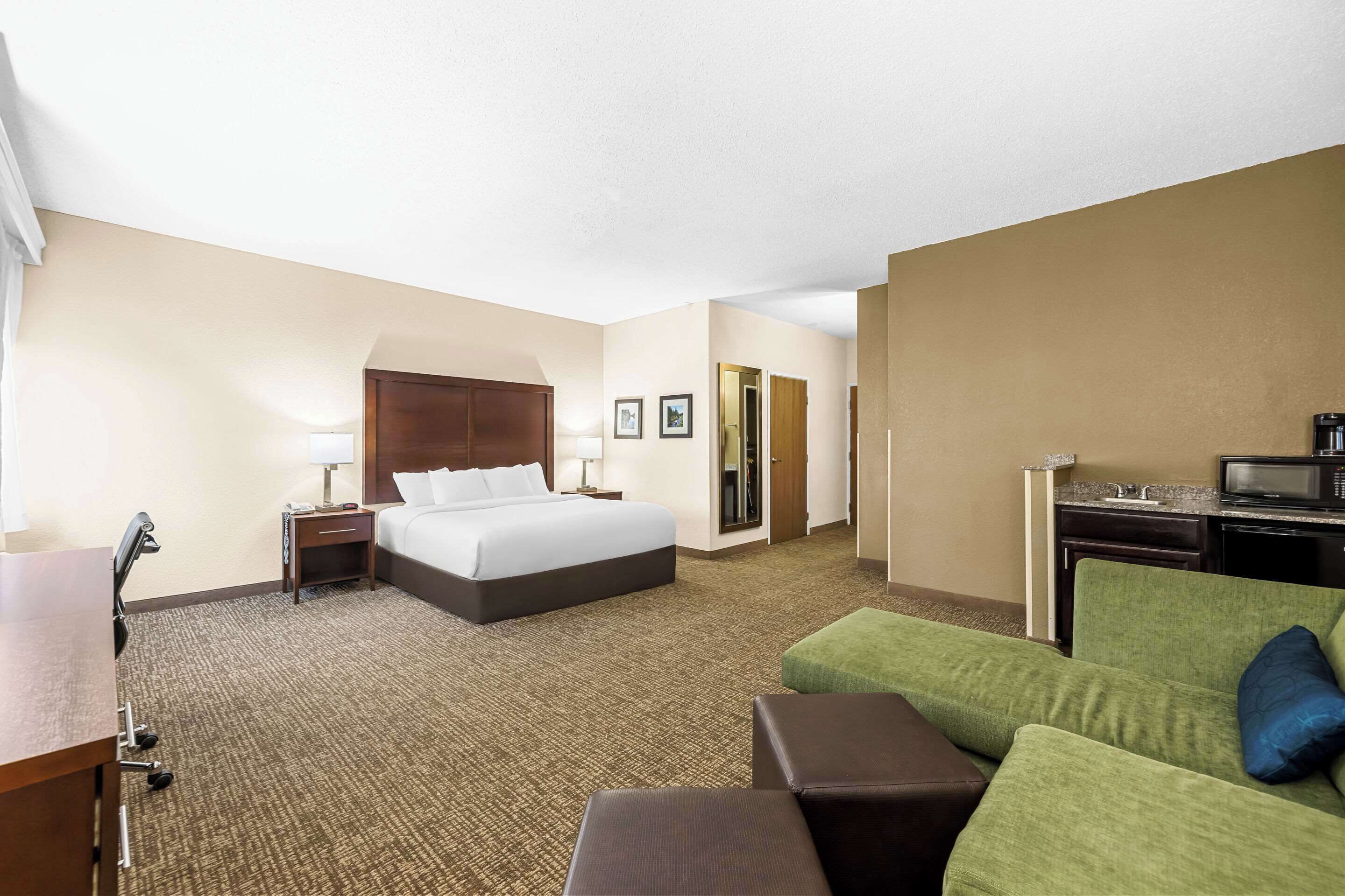 A hotel room with a bed, a desk, a green sofa, and a kitchenette.