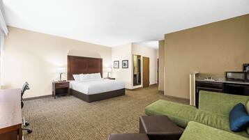 A hotel room with a bed, a desk, a green sofa, and a kitchenette.