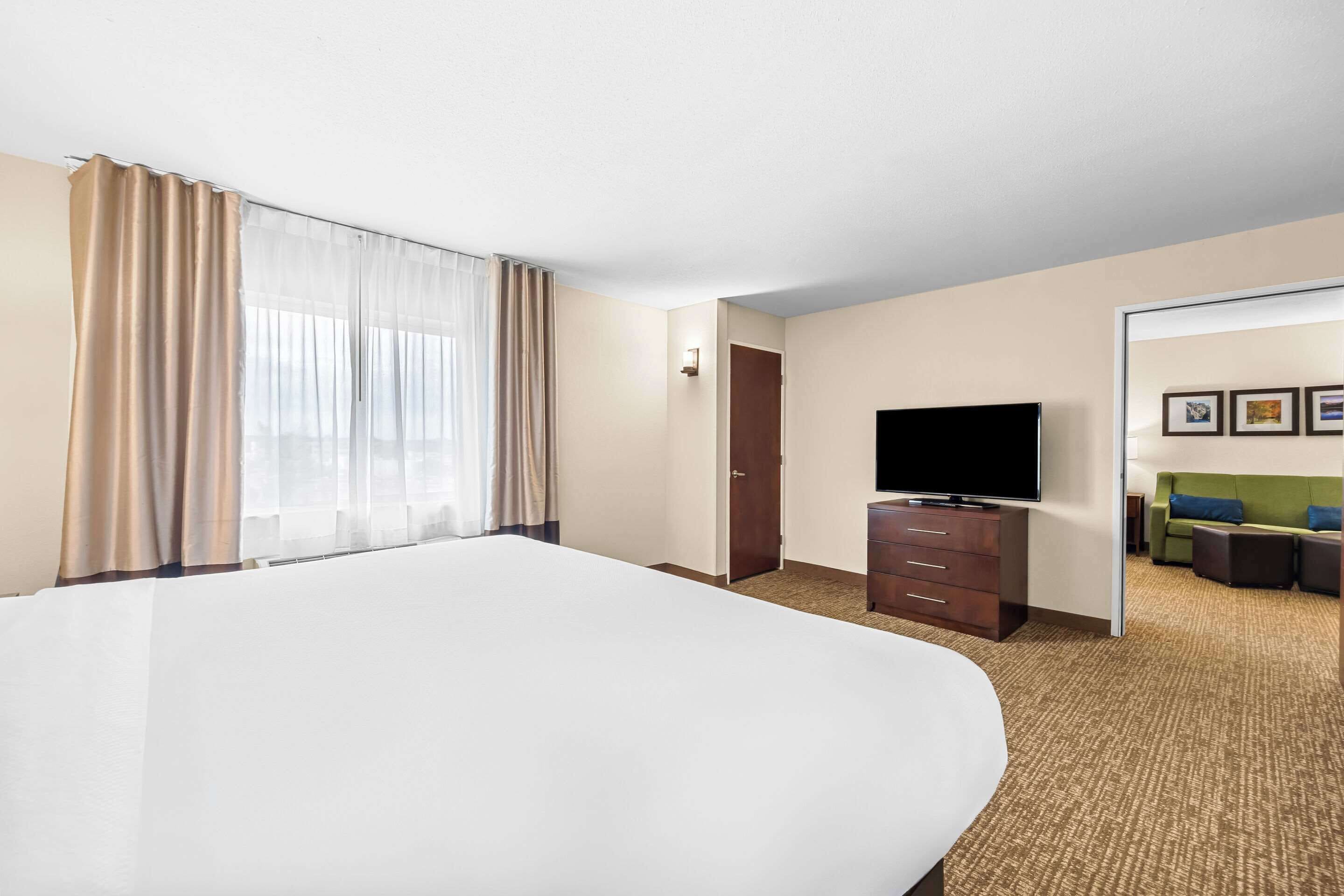 A hotel room with a large bed, a television, a dresser, and a sofa.