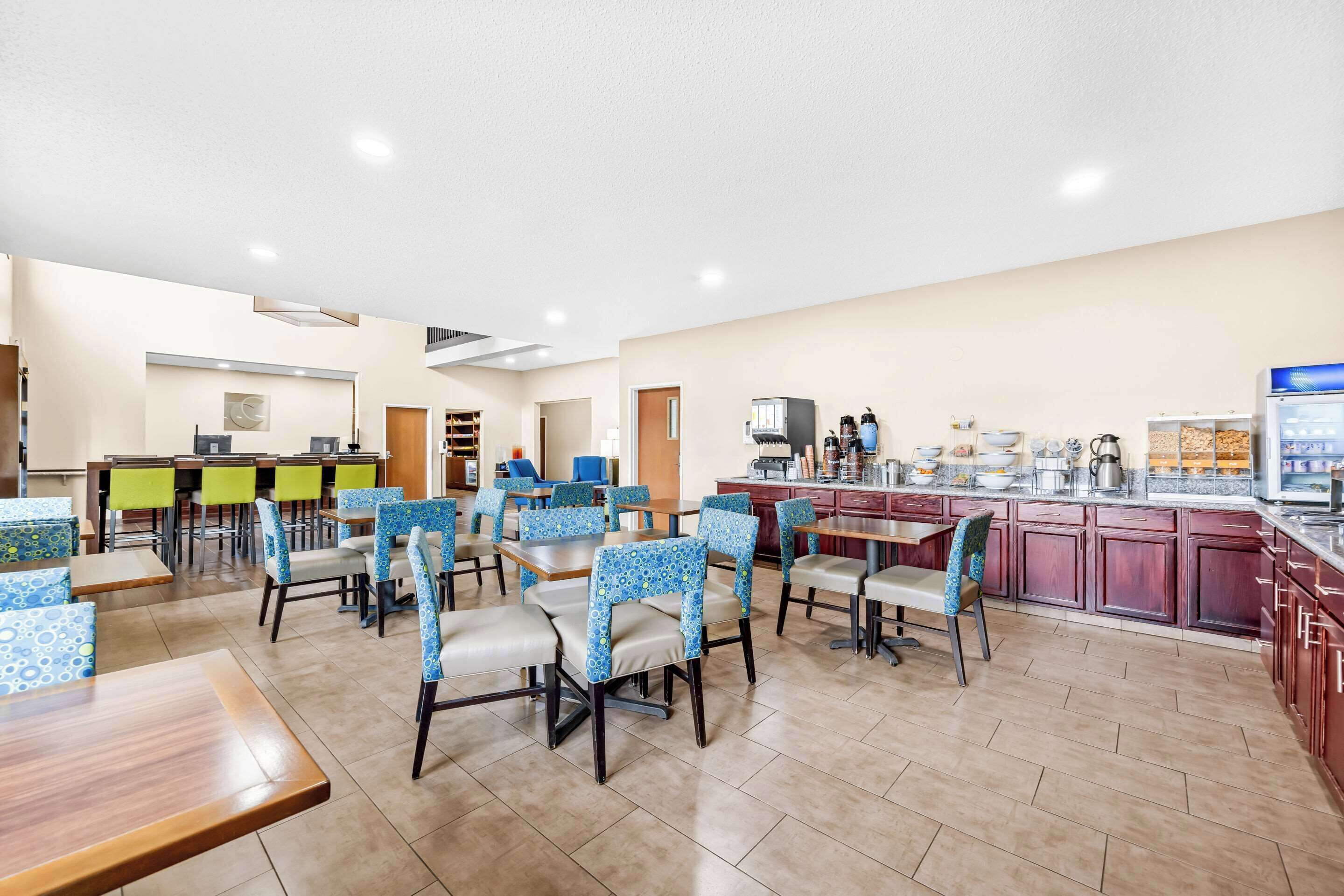 A hotel dining area with multiple tables and chairs, a kitchen area with appliances, and a counter with a coffee machine.