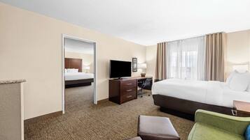 A hotel room with a bed, a desk with a computer, a television, and a seating area with a chair and ottoman.