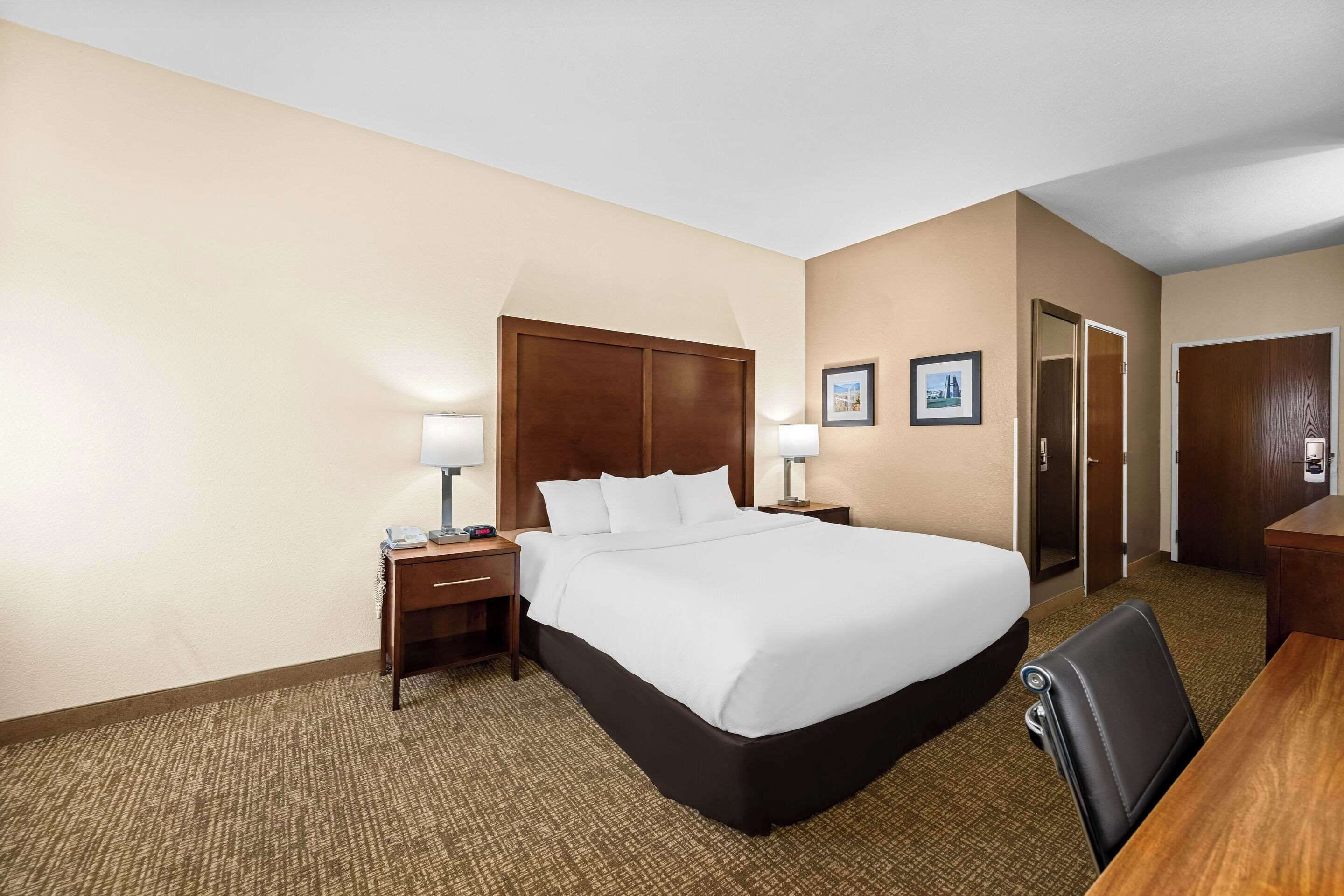 A hotel room with a large bed, a desk, a chair, two bedside tables with lamps, and a door.