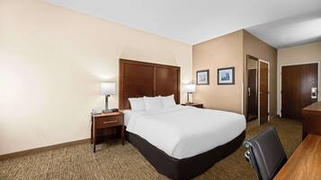 A hotel room with a large bed, a desk, a chair, two bedside tables with lamps, and a door.