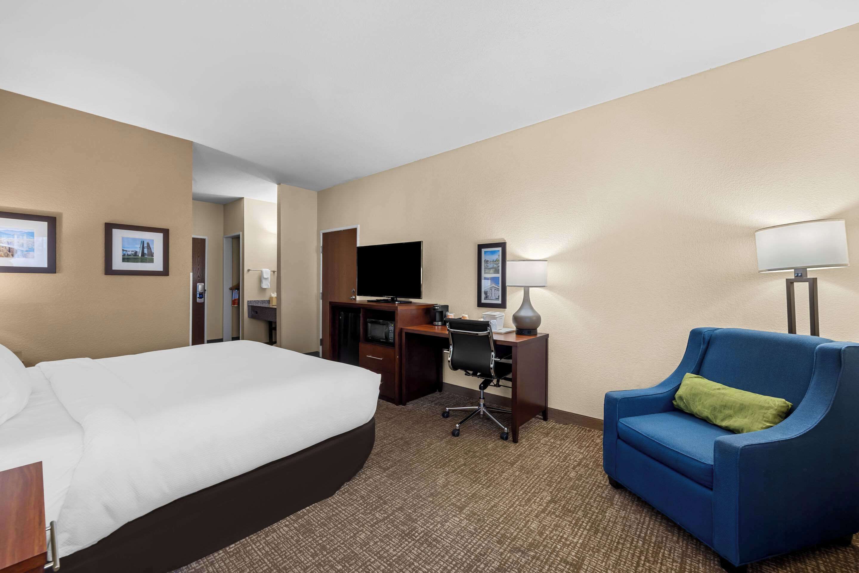 A hotel room with a large bed, a desk with a computer, a blue armchair, and a television.