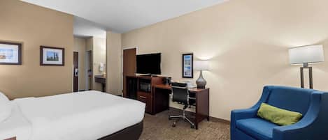 A hotel room with a large bed, a desk with a computer, a blue armchair, and a television.