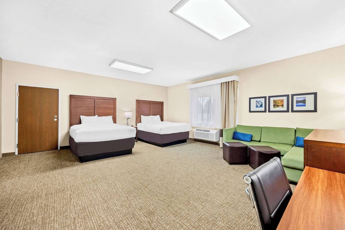 A hotel room with two beds, a green sofa, a wooden desk, and a window with curtains.