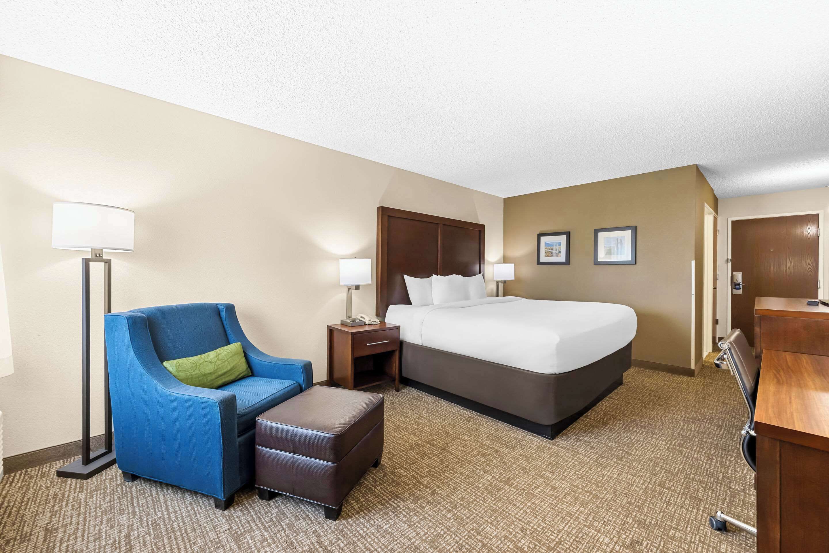 A hotel room with a bed, a blue armchair, a desk, and a lamp.