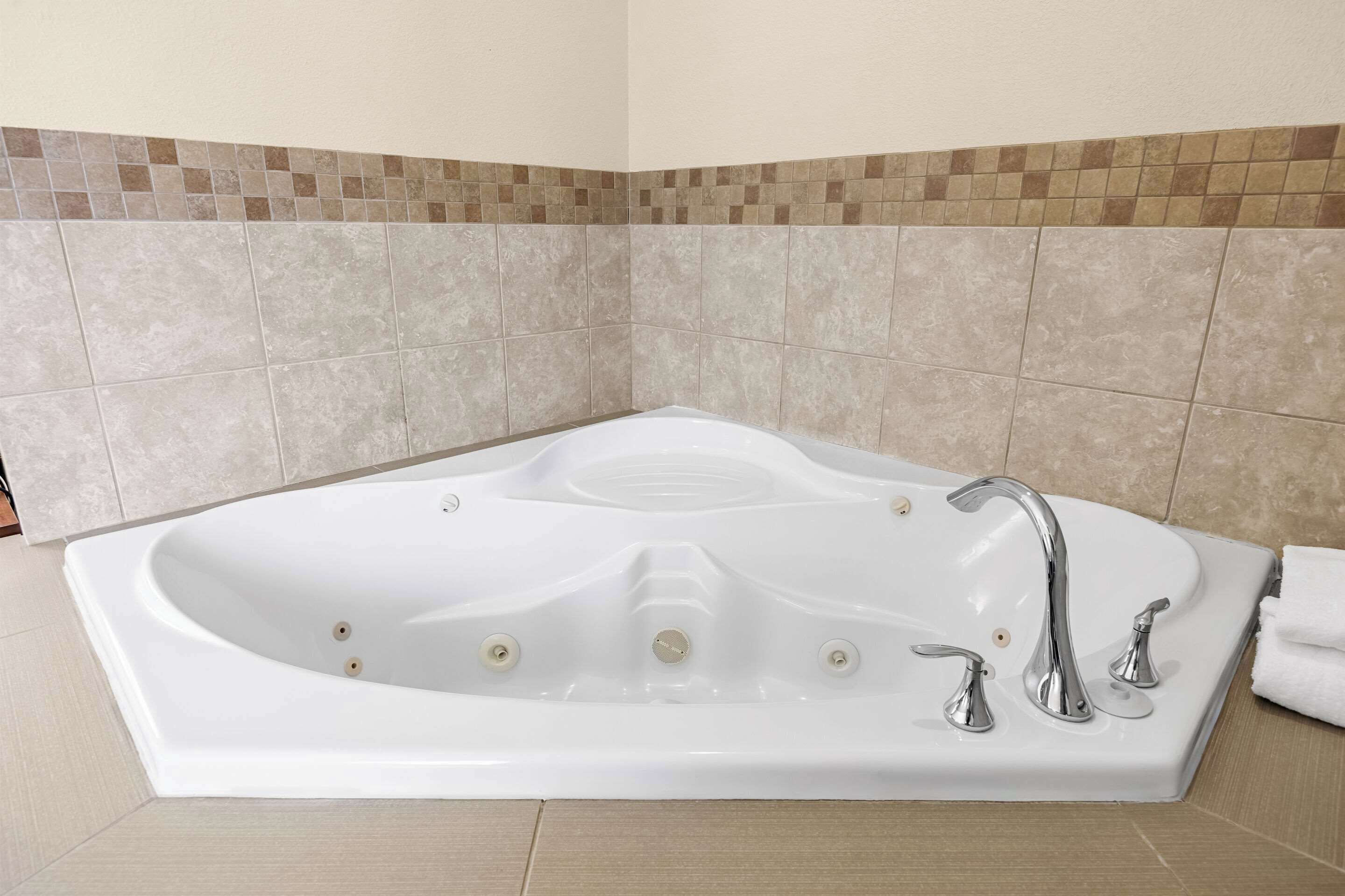 A large, rectangular bathtub with a single faucet and two control knobs, set against a tiled wall with a brown mosaic border.