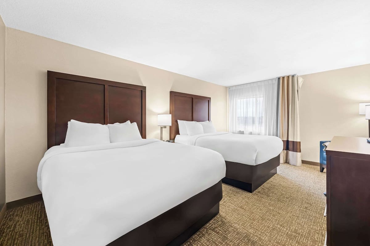 A hotel room with two beds, a desk, and a window with curtains.