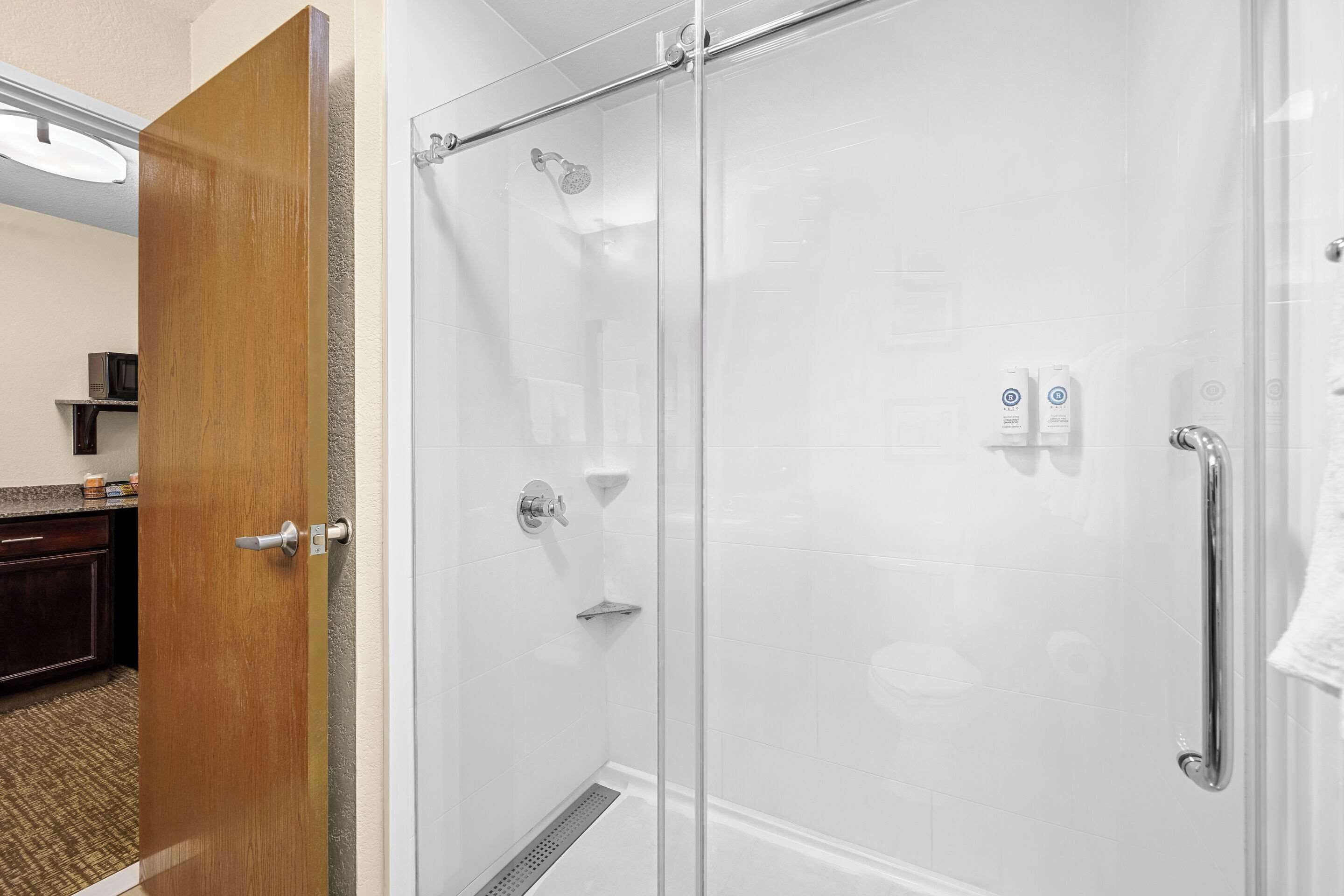 A glass-enclosed shower with a showerhead, a towel rack, and a soap dispenser.
