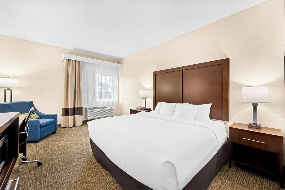 A hotel room with a large bed, a desk with a chair, a TV, and a window with curtains.