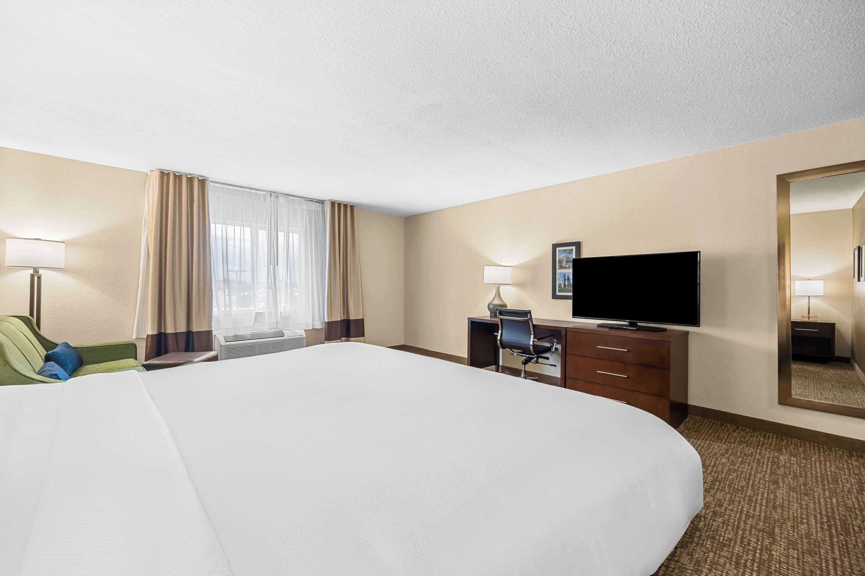 Une chambre d’hôtel avec un grand lit, un bureau avec une chaise, une télévision et un miroir.