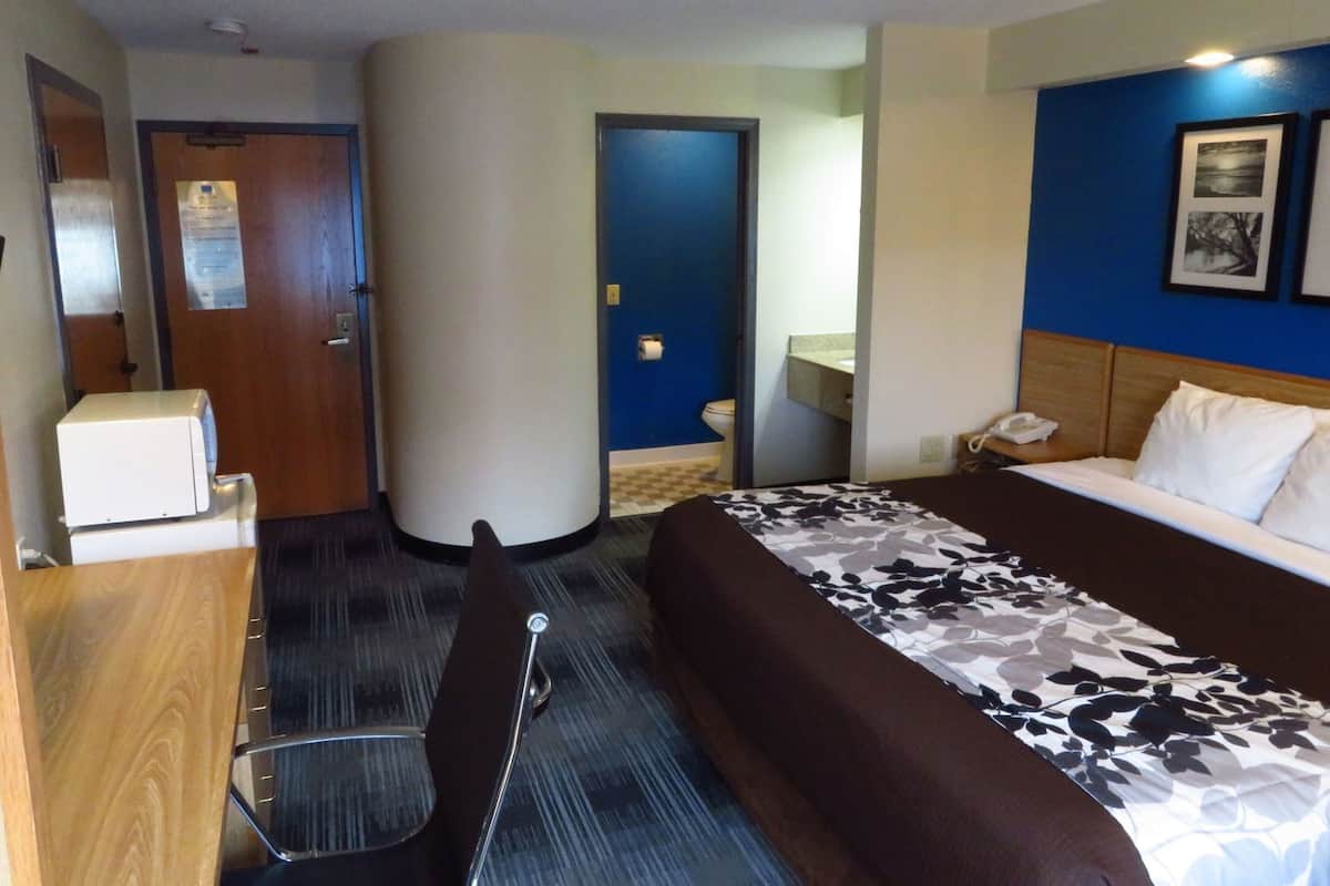 A hotel room with a bed, a desk, a chair, a telephone, and a bathroom visible through an open door.