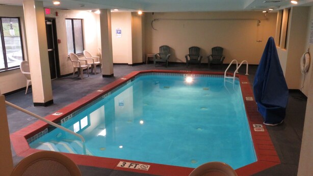 An indoor swimming pool with a 3 FT depth marker, surrounded by chairs and a covered bench. - Rodeway Inn Austell Six Flags (Austell)