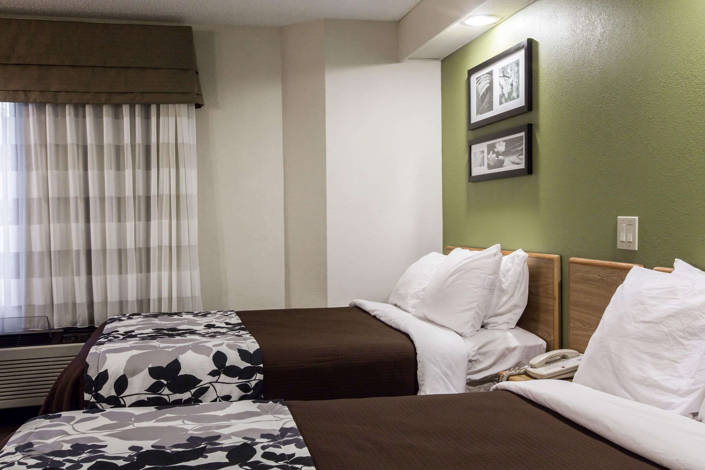 A hotel room with two beds, a window with curtains, a wall-mounted phone, and framed pictures.